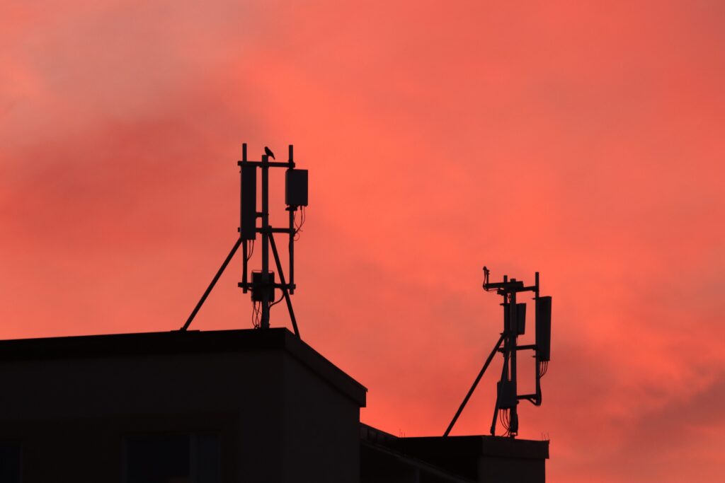 Silhouetted antennas on building roof against an orange sunset sky creating a striking scene.