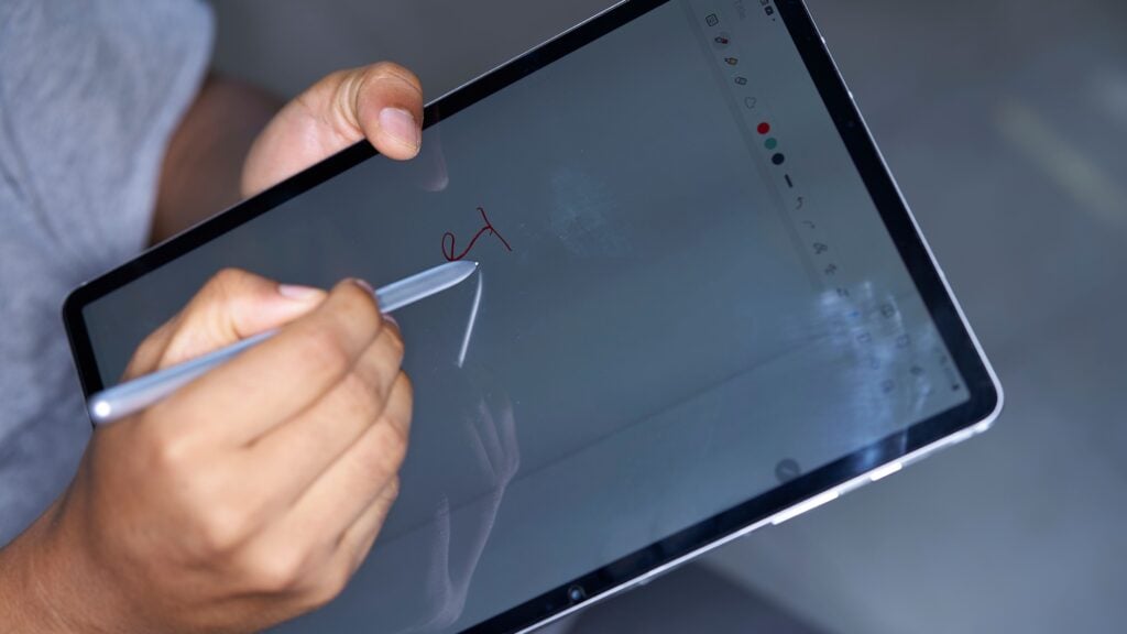 A person writes on a digital tablet using a stylus, highlighting modern technology and creativity.