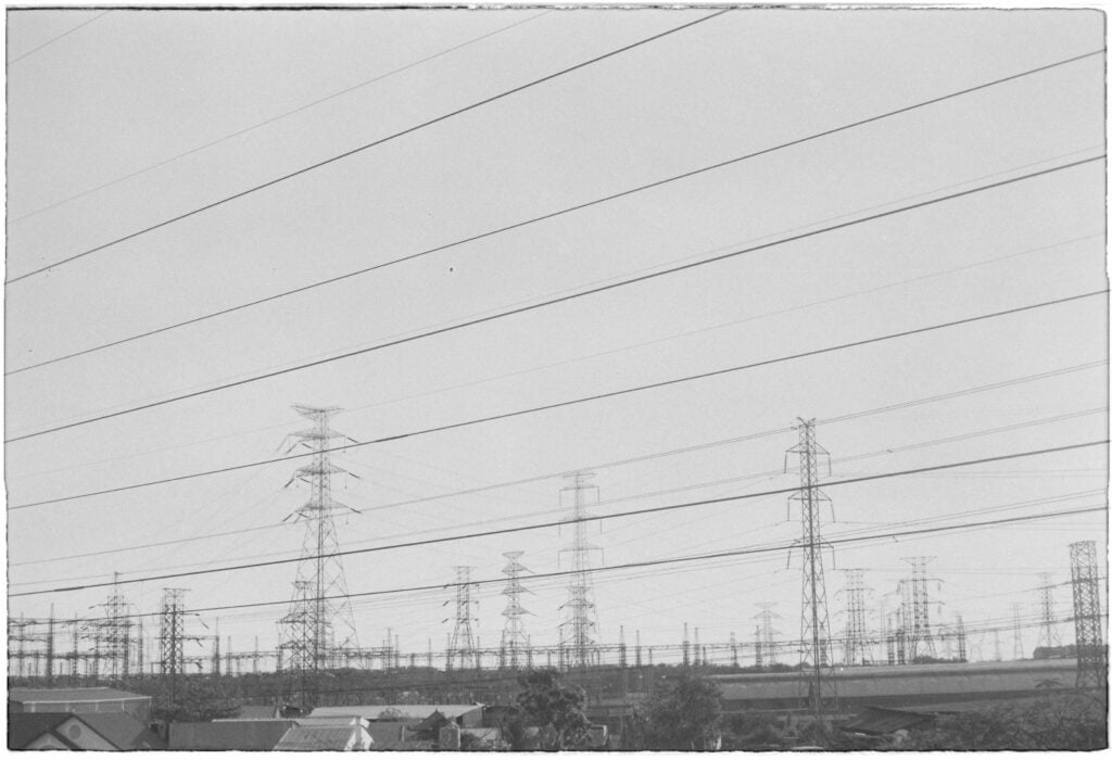 Monochrome image of rows of power lines and pylons in an industrial zone.