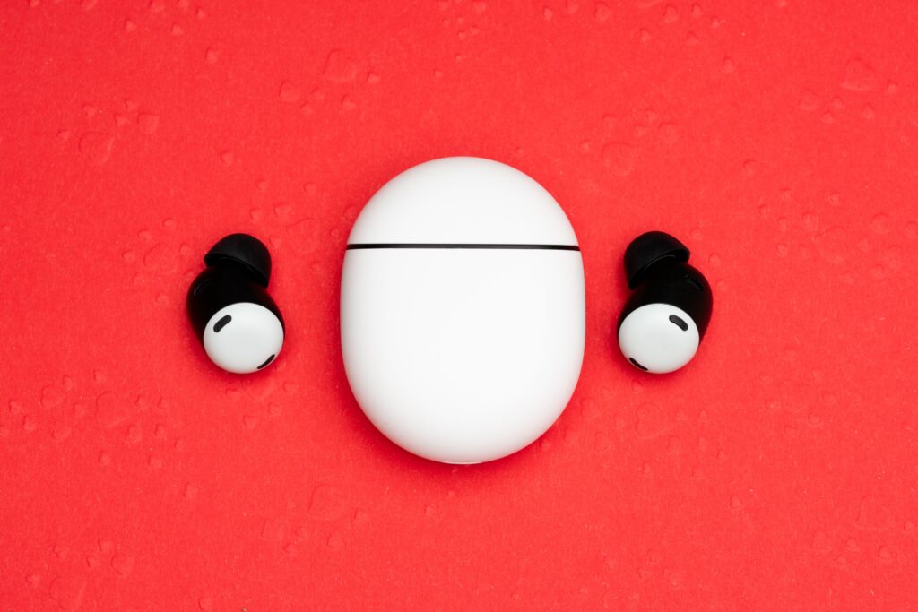 Top view of white wireless earbuds with charging case on a vibrant red background.