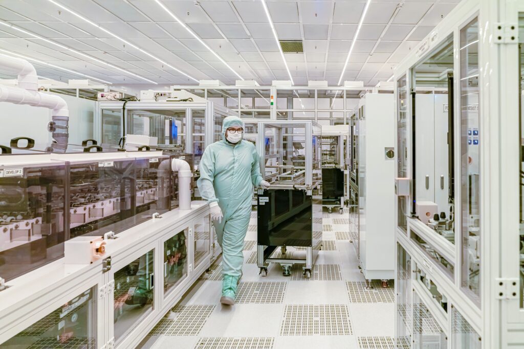 Scientist in protective gear walking in a high-tech cleanroom laboratory environment.
