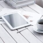 White tablet with stylus and coffee cup on modern office desk setup.