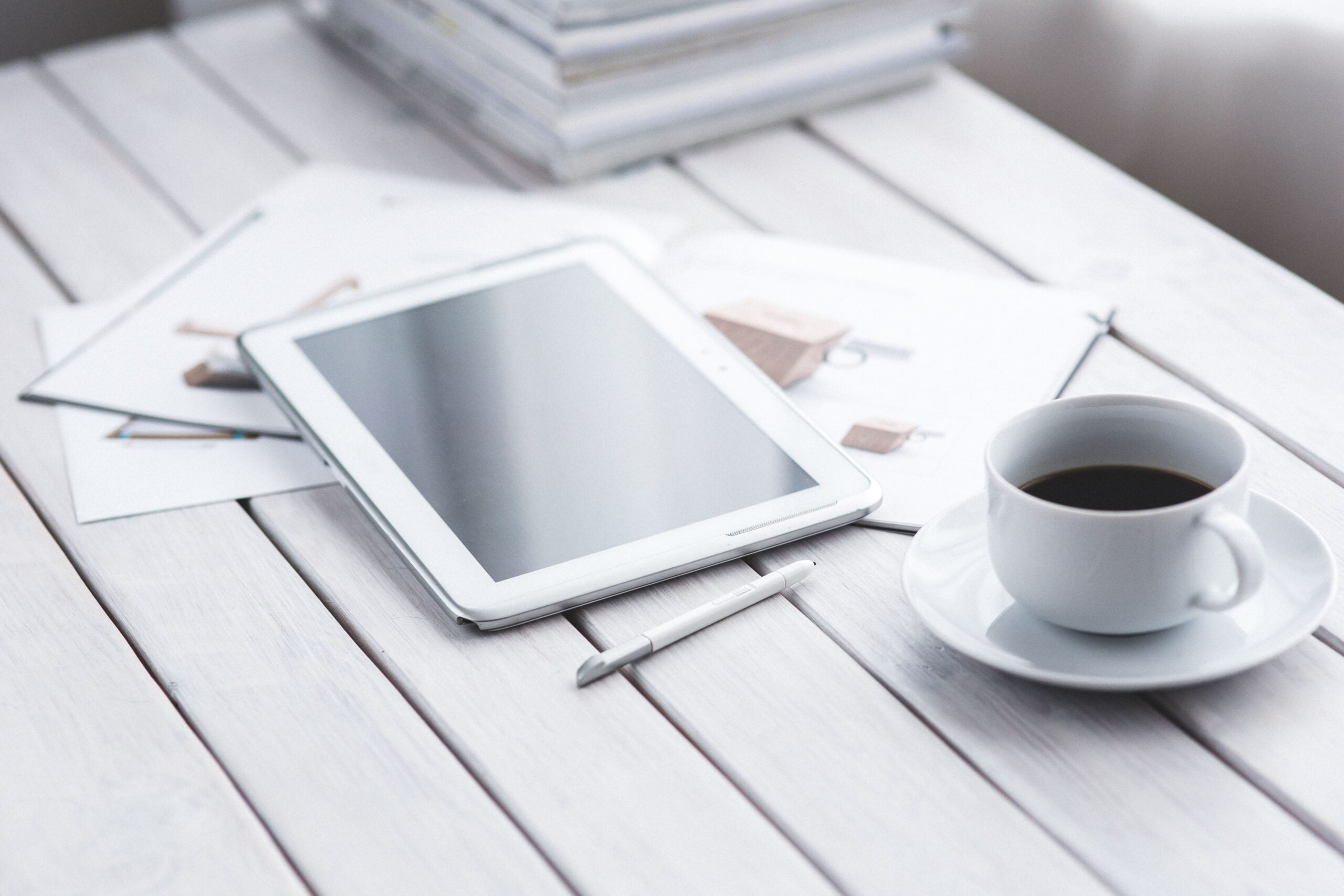 White tablet with stylus and coffee cup on modern office desk setup.