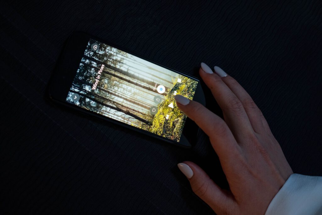 A hand interacting with a smartphone displaying a forest-themed app on a dark surface.