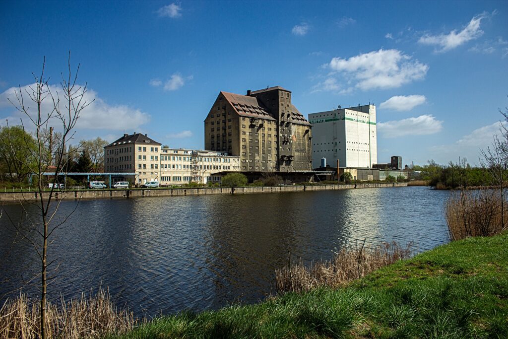 Riverside industrial buildings against a clear blue sky in Leipzig, Germany.