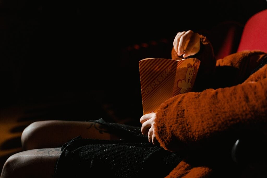 A person enjoying popcorn during a movie at an indoor cinema, sitting comfortably.
