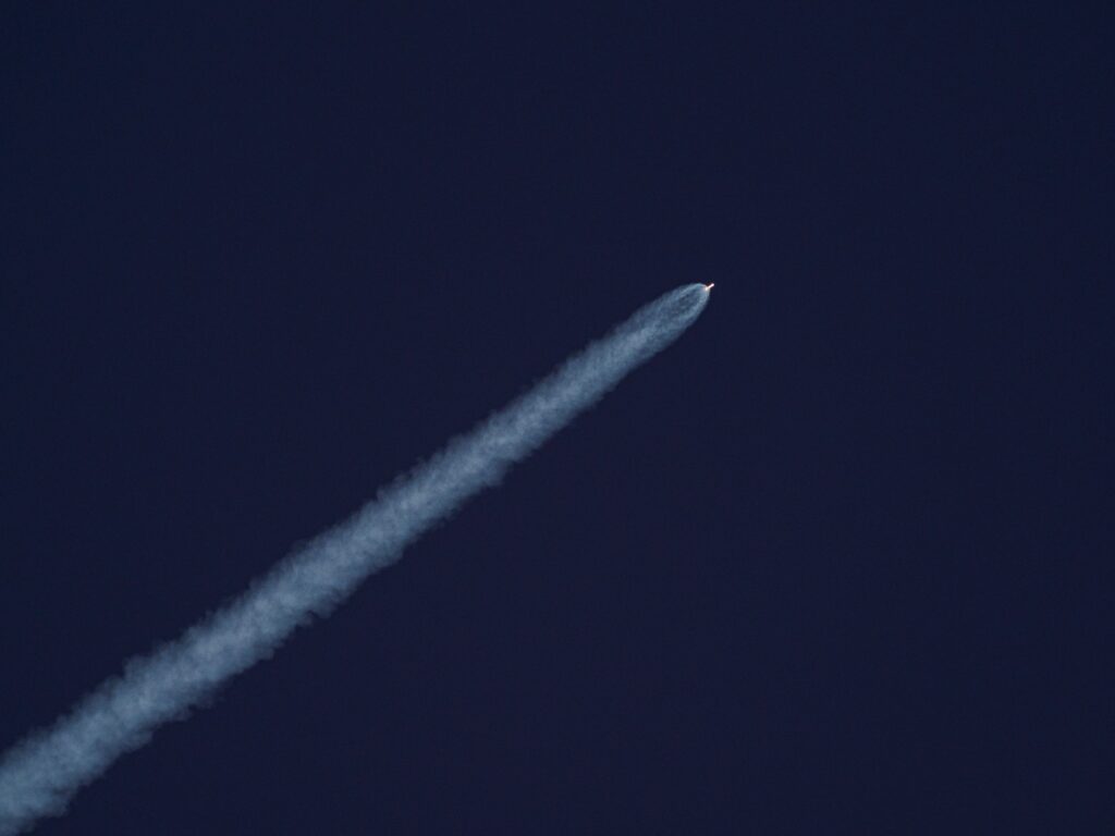 A rocket ascends into the sky, leaving a trail of smoke against the clear blue sky.