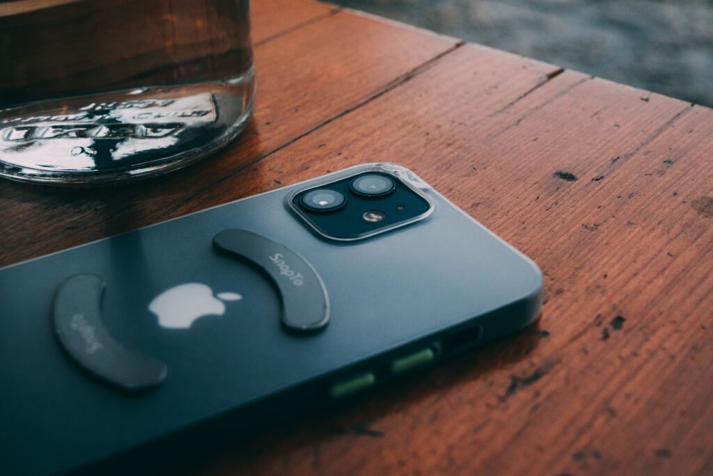 A sleek smartphone lies on a rustic wooden table beside a glass object, showcasing modern technology.