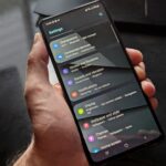 Hand holding smartphone displaying settings screen with various options evident.