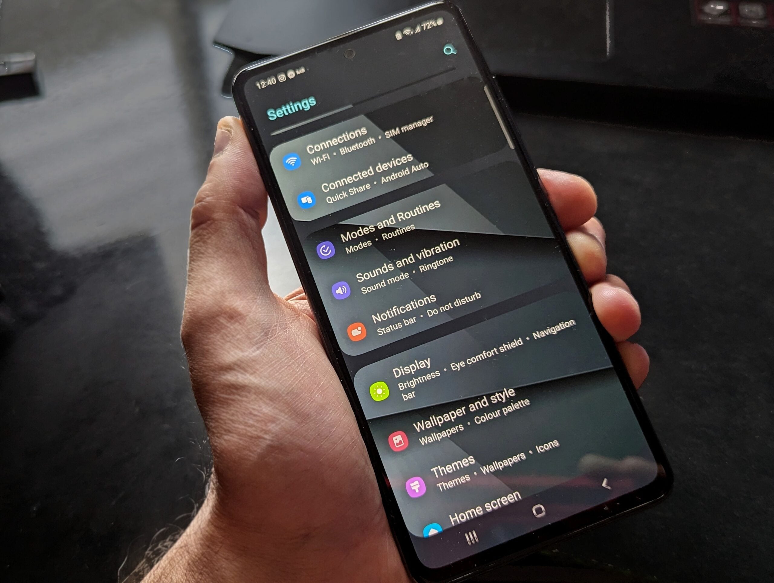 Hand holding smartphone displaying settings screen with various options evident.