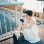 Woman in a white dress cools down with a portable fan on a sunny day outdoors.