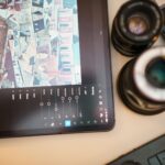A modern workspace featuring a tablet editing cityscape photo, camera lens, and keyboard.