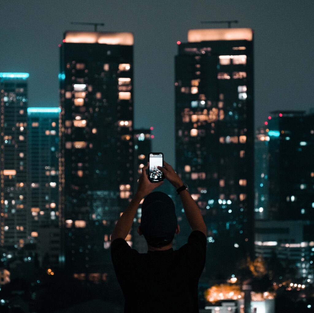 A person photographing Jakarta's illuminated skyscrapers during a vibrant city night.