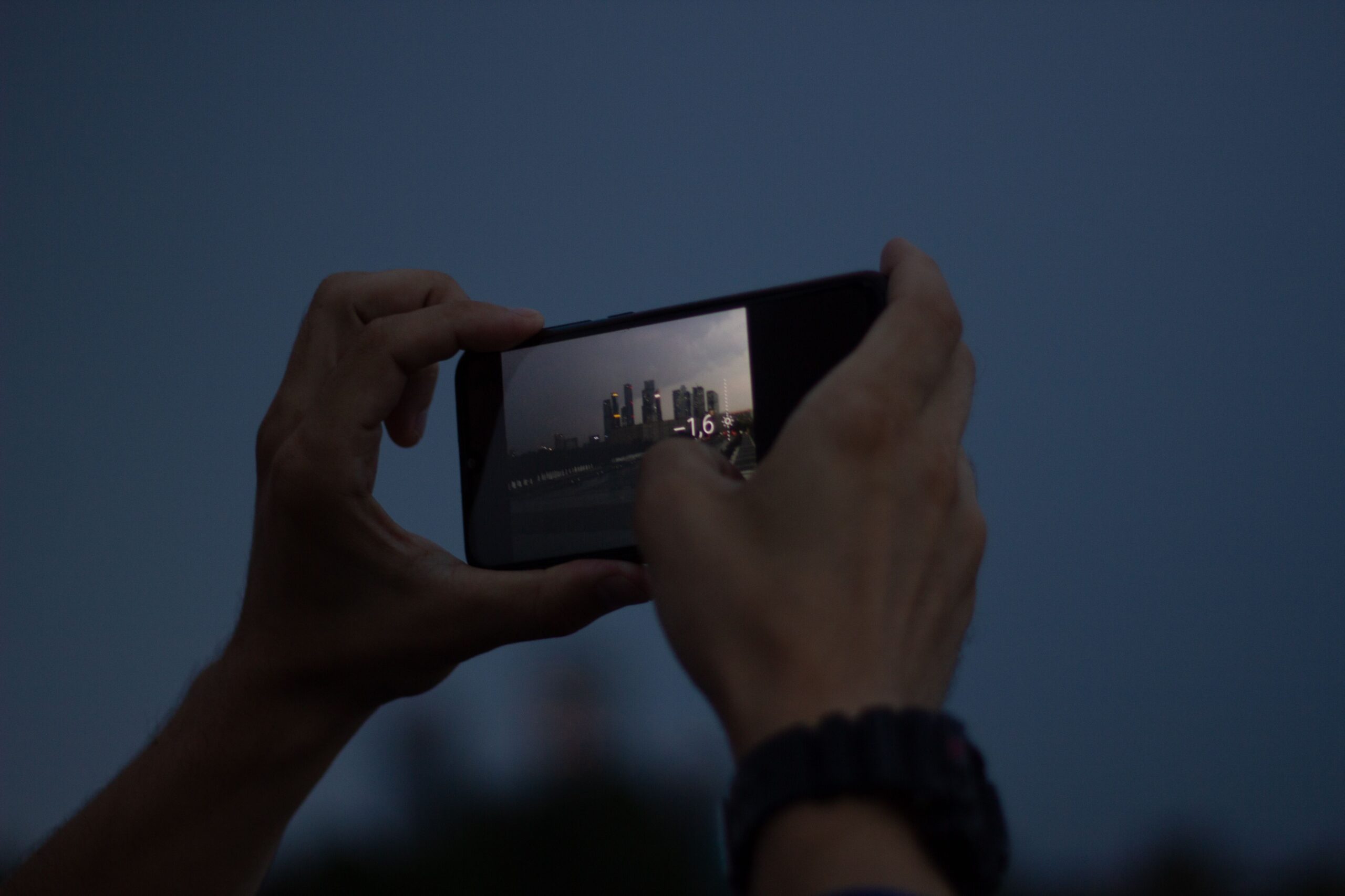 A person capturing a city skyline with a smartphone during twilight, showcasing urban photography.